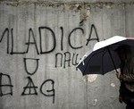 Žena prochází kolem grafitu "S Mladićem do Haagu"